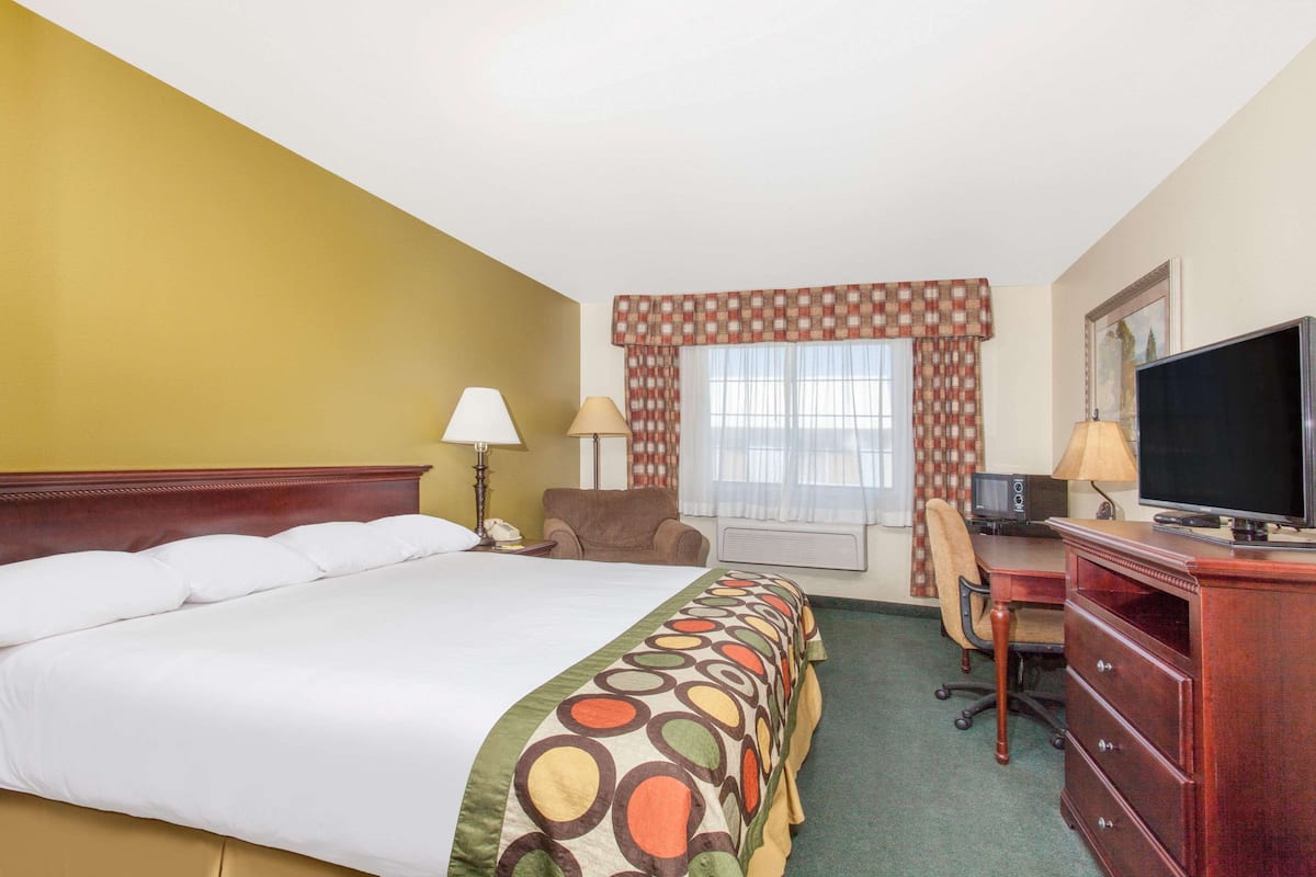 A hotel room with a bed, desk, chair, television, and a window with curtains.