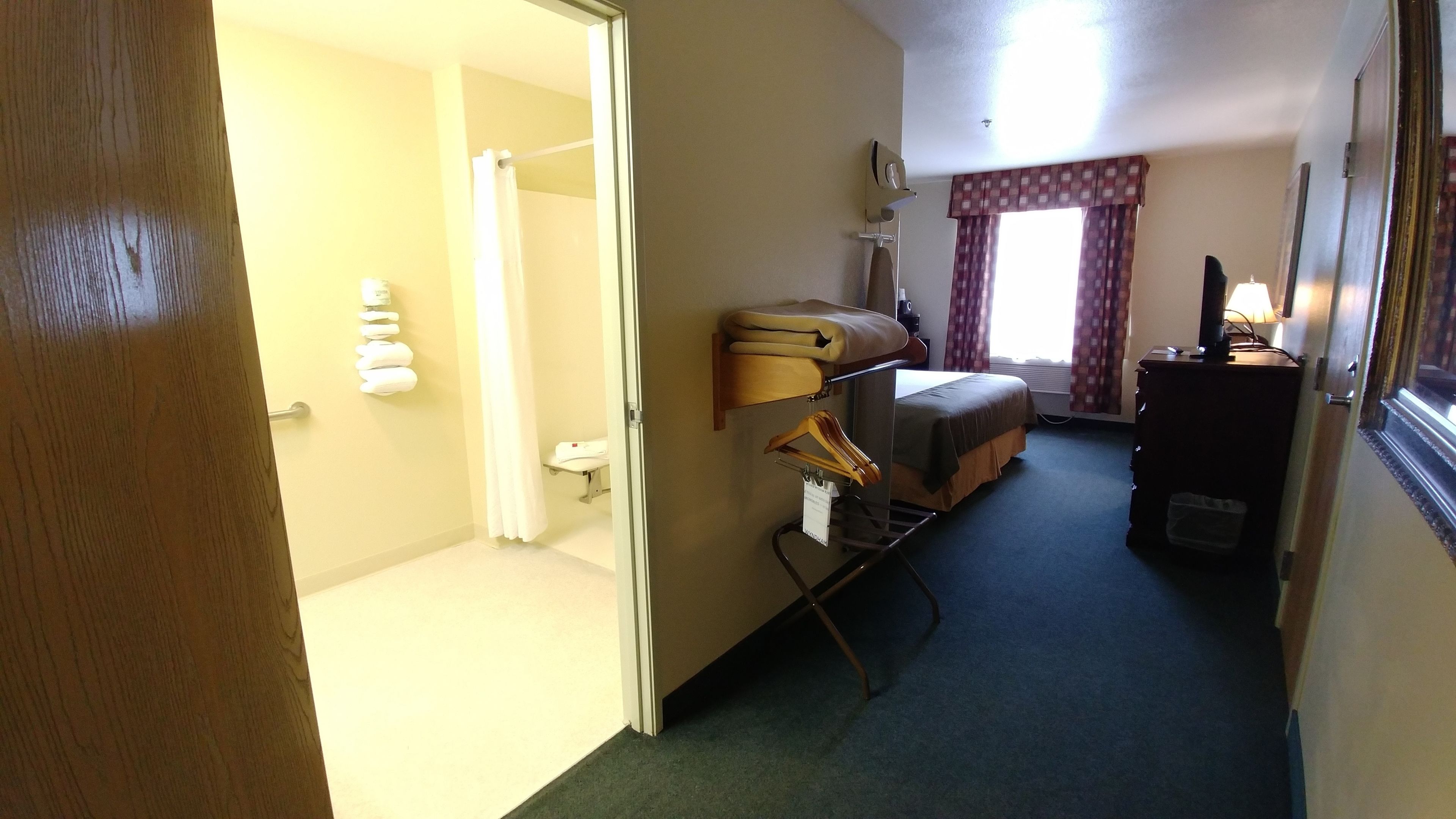 A hotel room with a bed, a desk, a chair, a wardrobe, and a window with curtains.