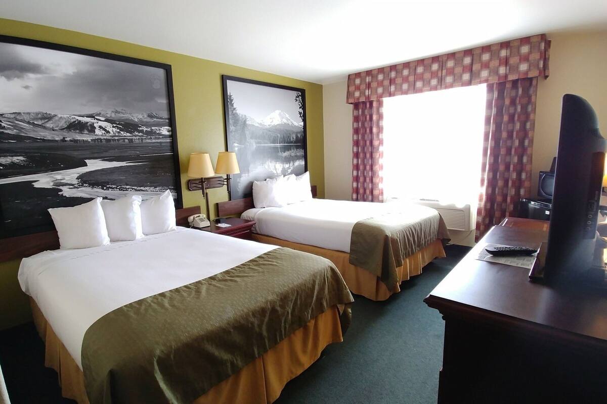 A hotel room with two beds, a desk with a computer, a TV, and a window with curtains.
