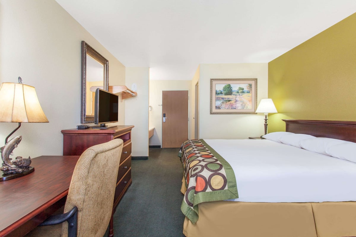 A hotel room with a bed, a desk with a computer, a chair, a dresser, and a painting on the wall.