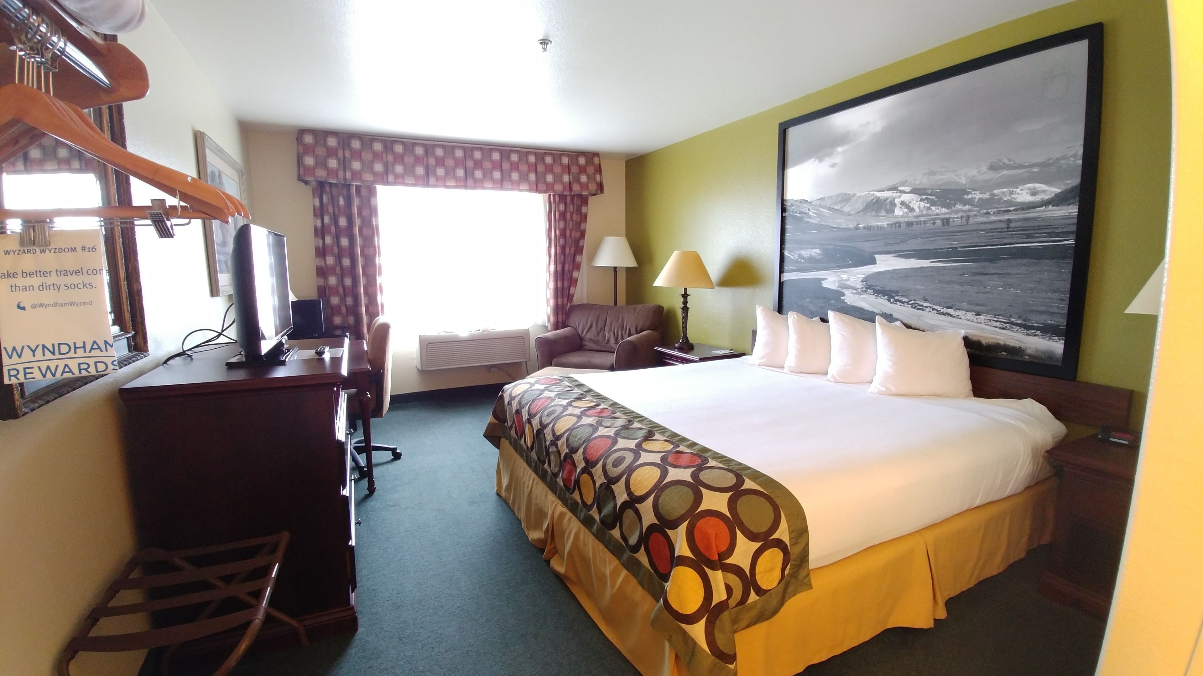 A hotel room with a bed, desk, chair, and a large window with curtains.
