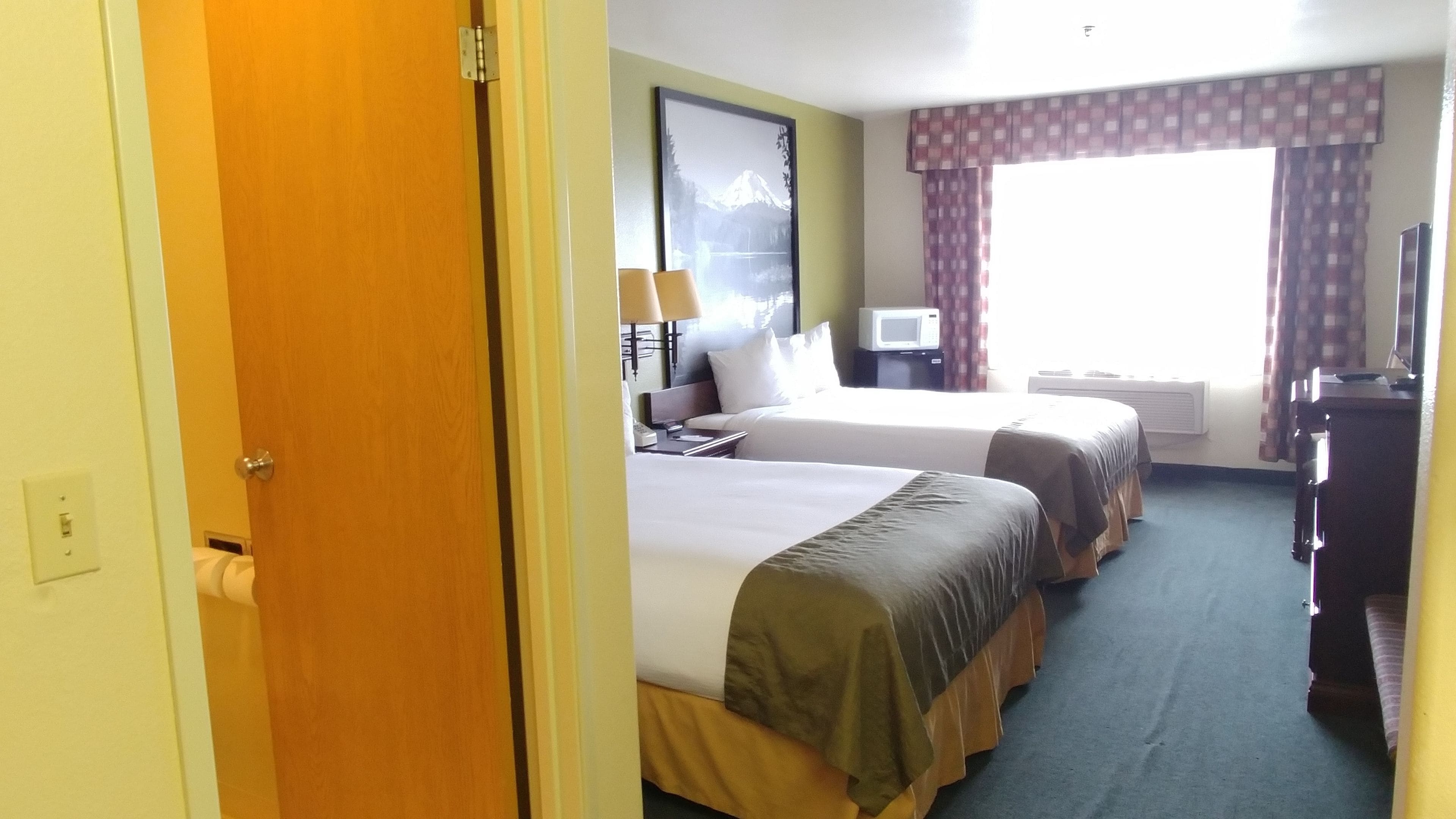 Una camera d'albergo con due letti, una scrivania, una sedia, una televisione e una finestra con tende.