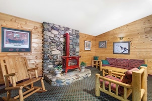 Interior de una cabaña de troncos con chimenea de piedra, muebles de madera y cuadros en las paredes.