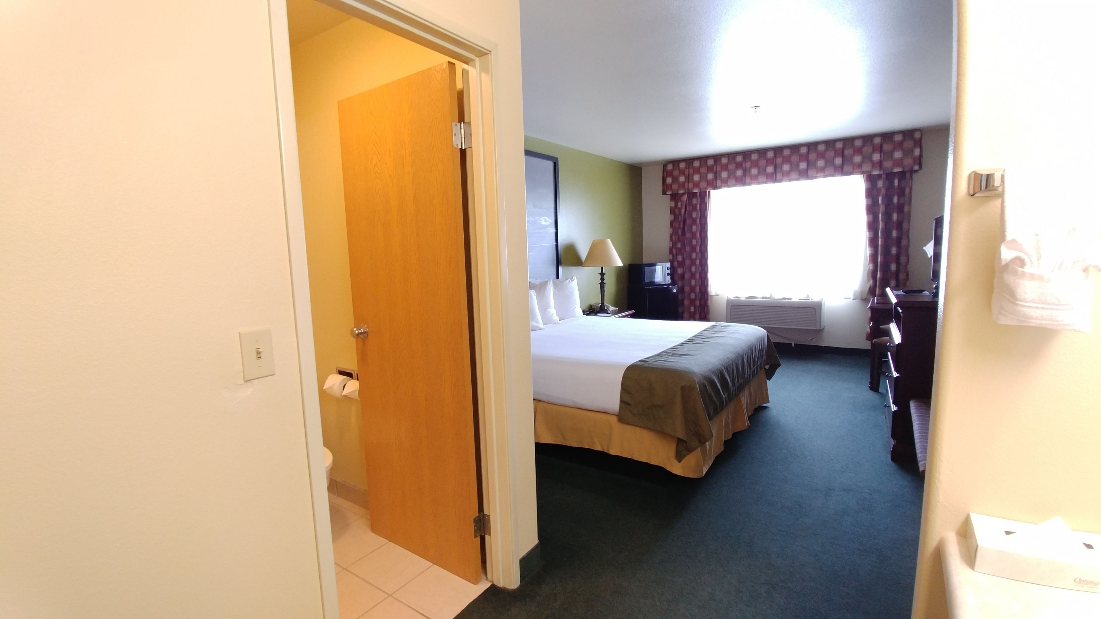 A hotel room with a bed, a desk, a chair, a lamp, and a window with curtains.