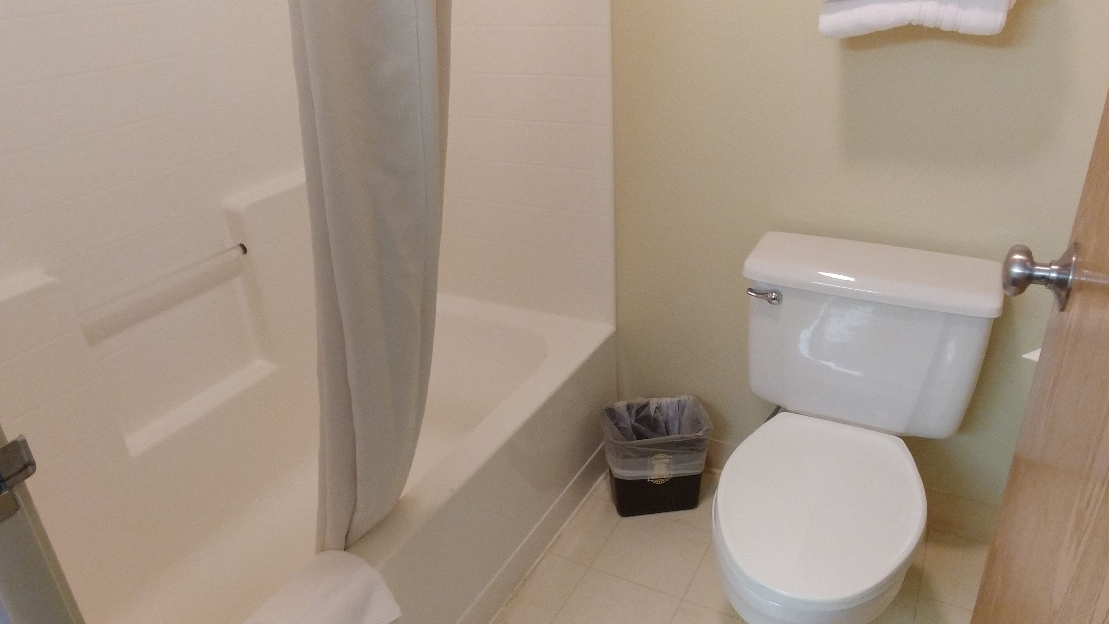 A small bathroom with a toilet, a shower curtain, and a trash bin.