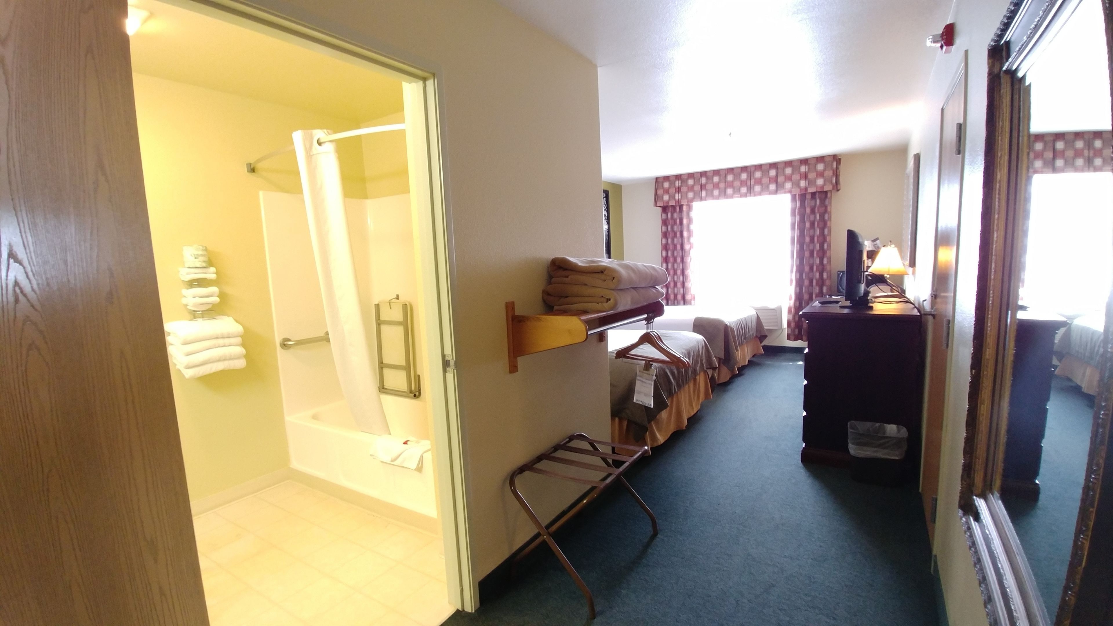 Habitación de hotel con ducha, cama con cabecero de madera, escritorio con lámpara y espejo.
