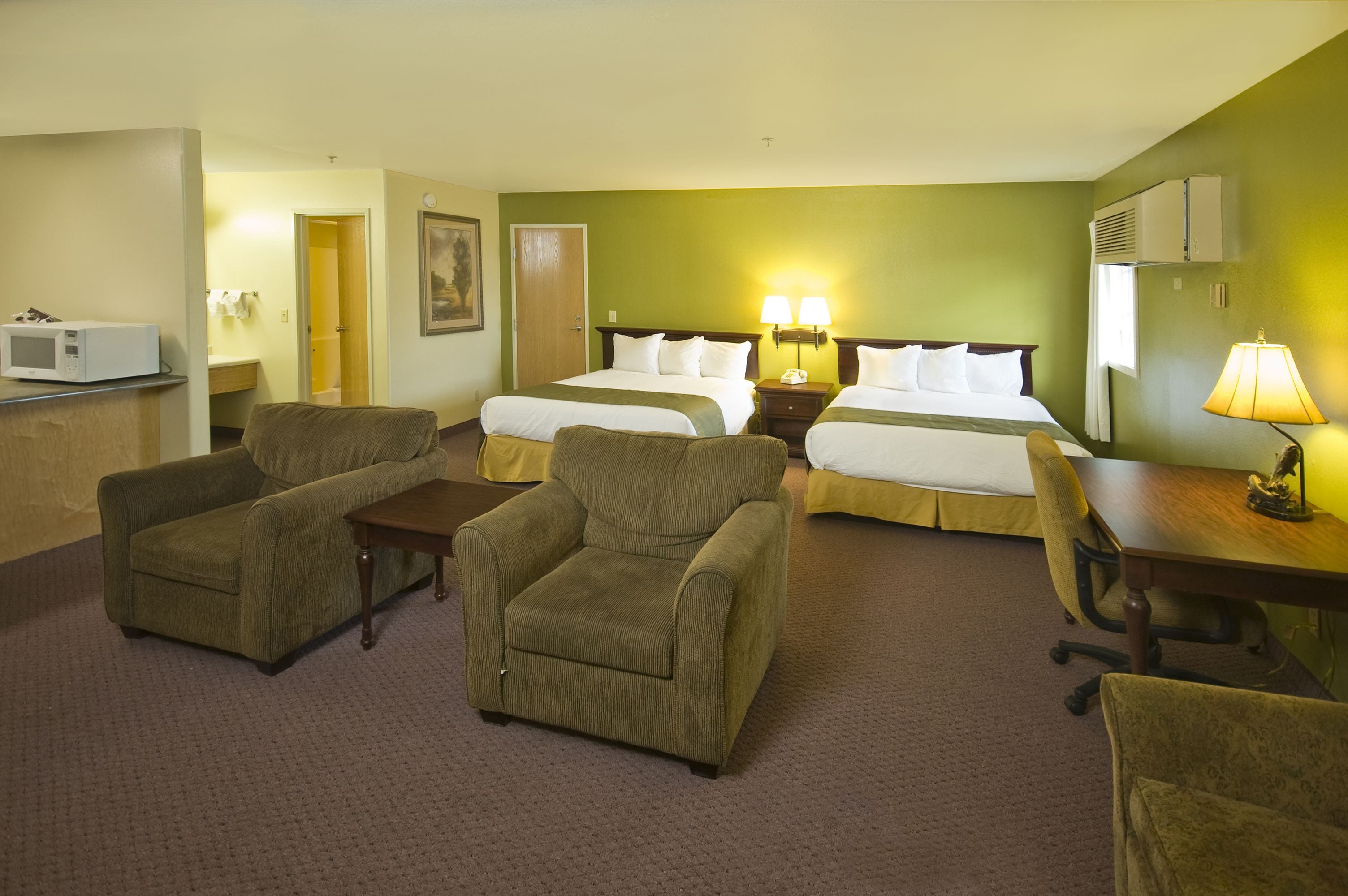 A hotel room with two beds, a desk, a chair, a microwave, and a lamp.