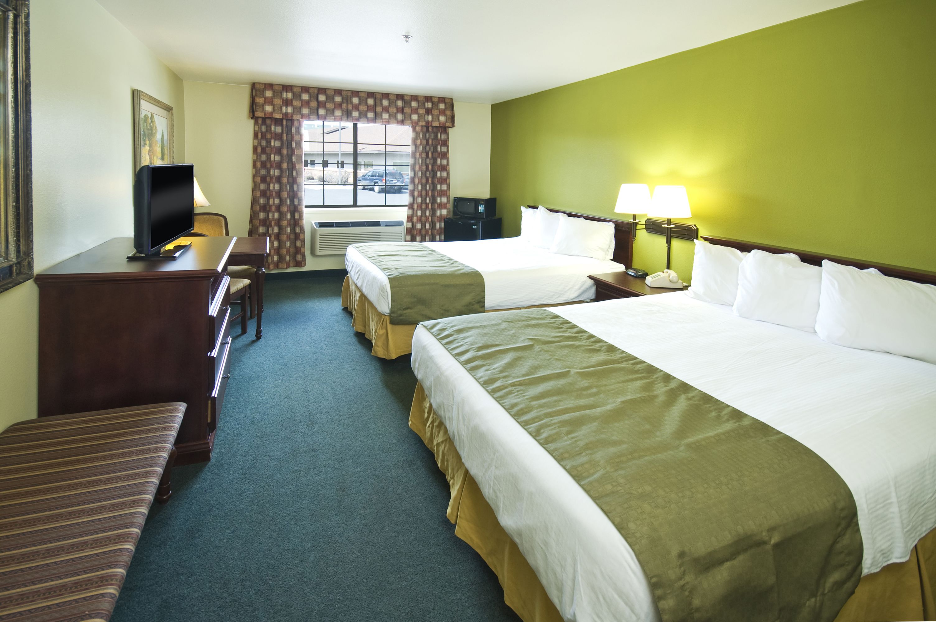 Ein Hotelzimmer mit zwei Betten, einem Schreibtisch mit Fernseher, einem Stuhl und einem Fenster mit Vorhängen.