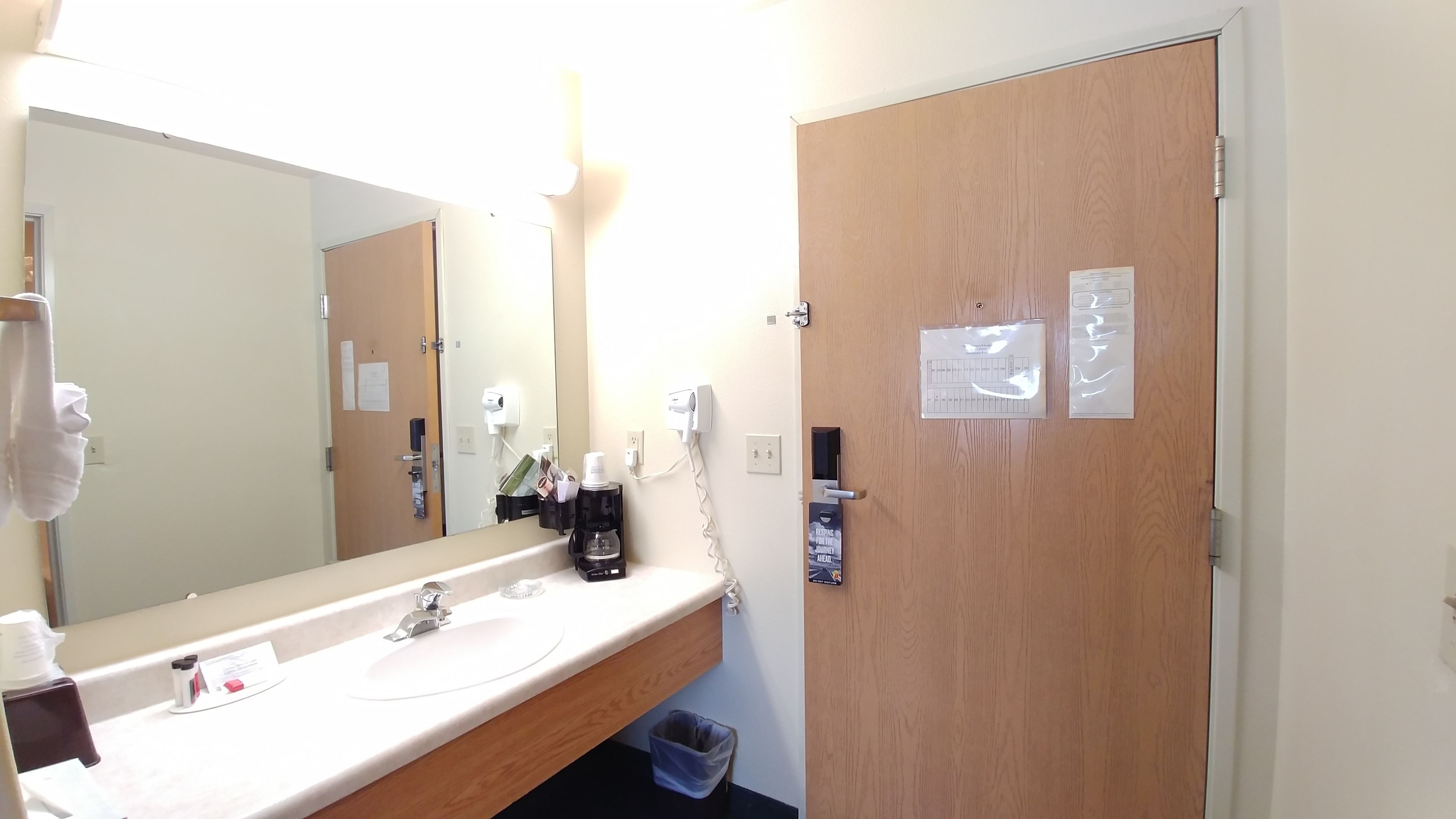 A hotel bathroom with a sink, mirror, and wooden door.