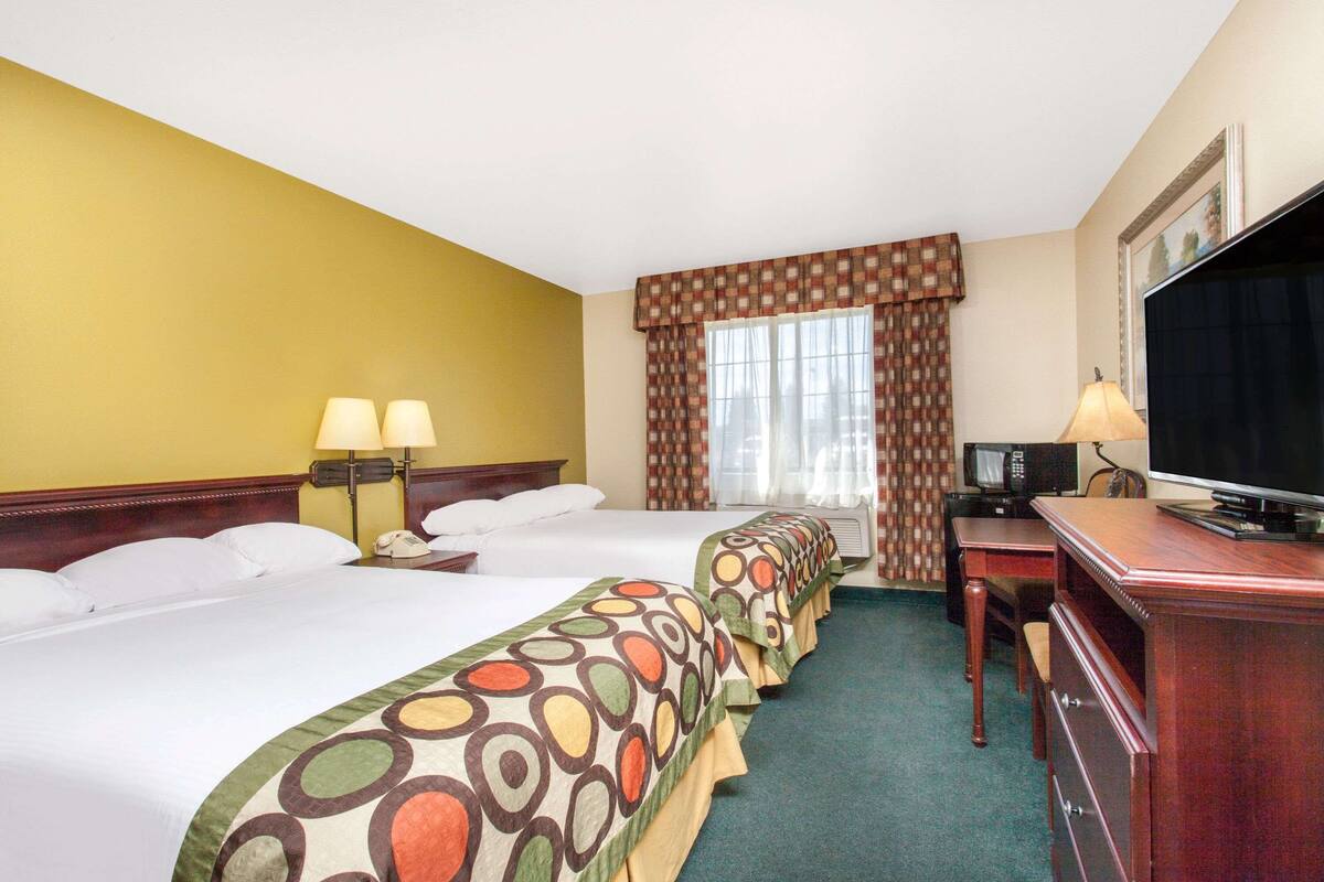 A hotel room with three beds, a desk with a television, and two lamps.