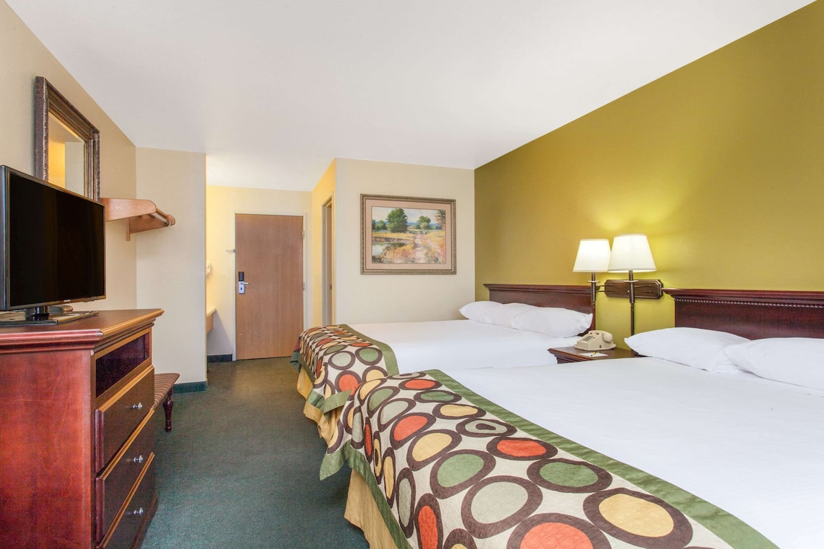 A hotel room with two beds, a TV, a desk, and a lamp.