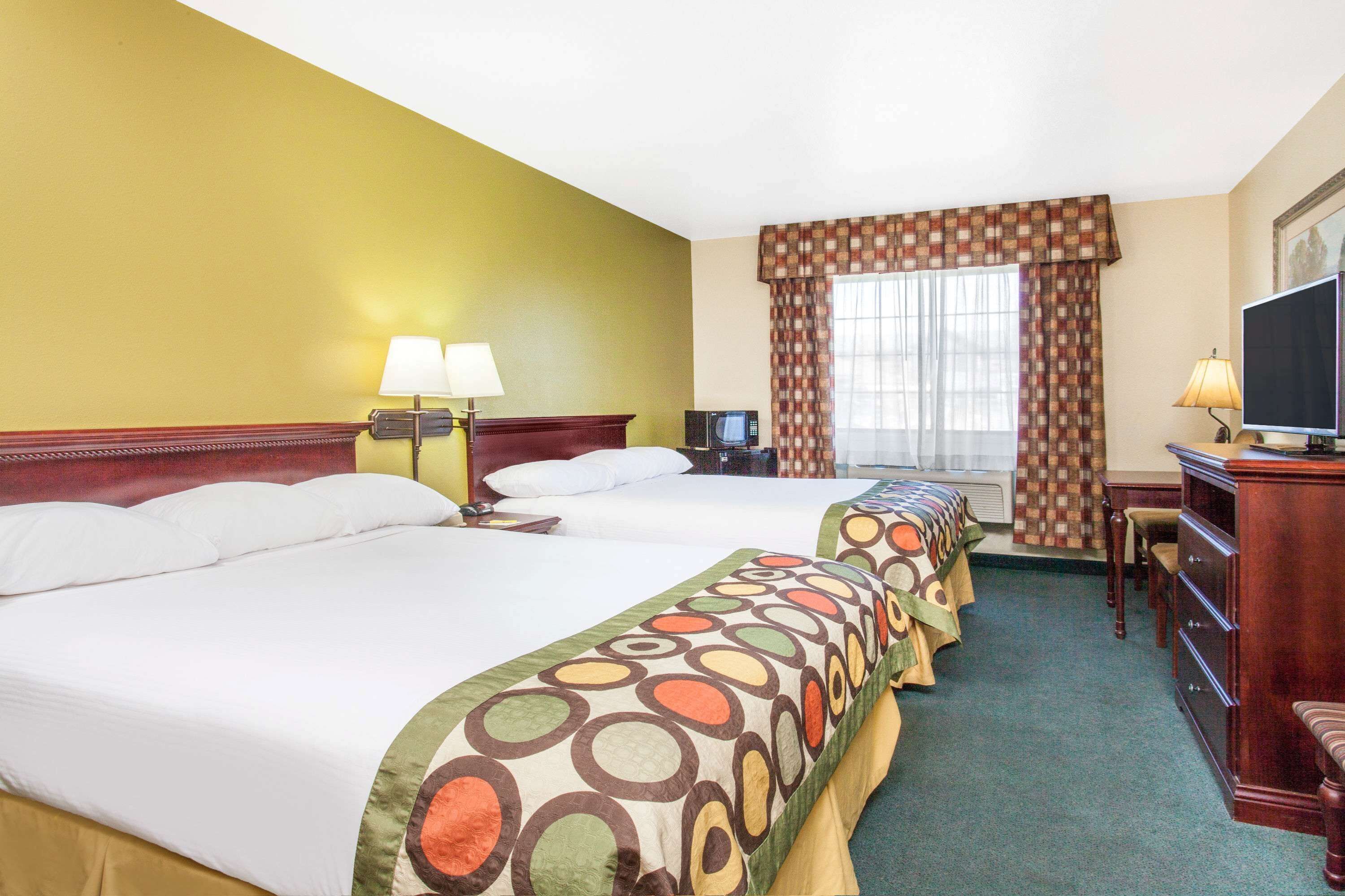 A hotel room with two beds, a desk, a television, and a window with curtains.