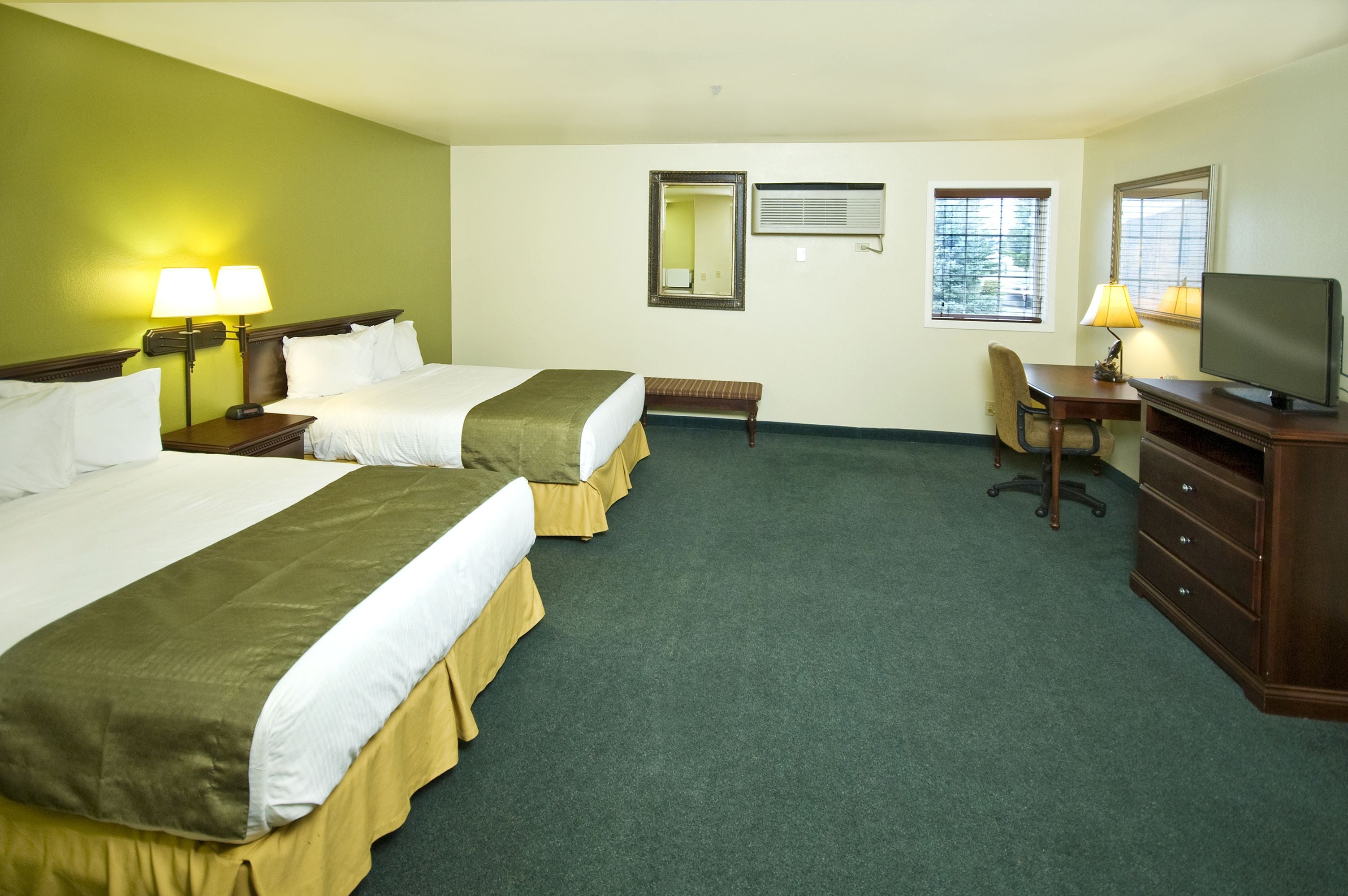 A hotel room with two beds, a desk, a chair, a television, and a mirror.