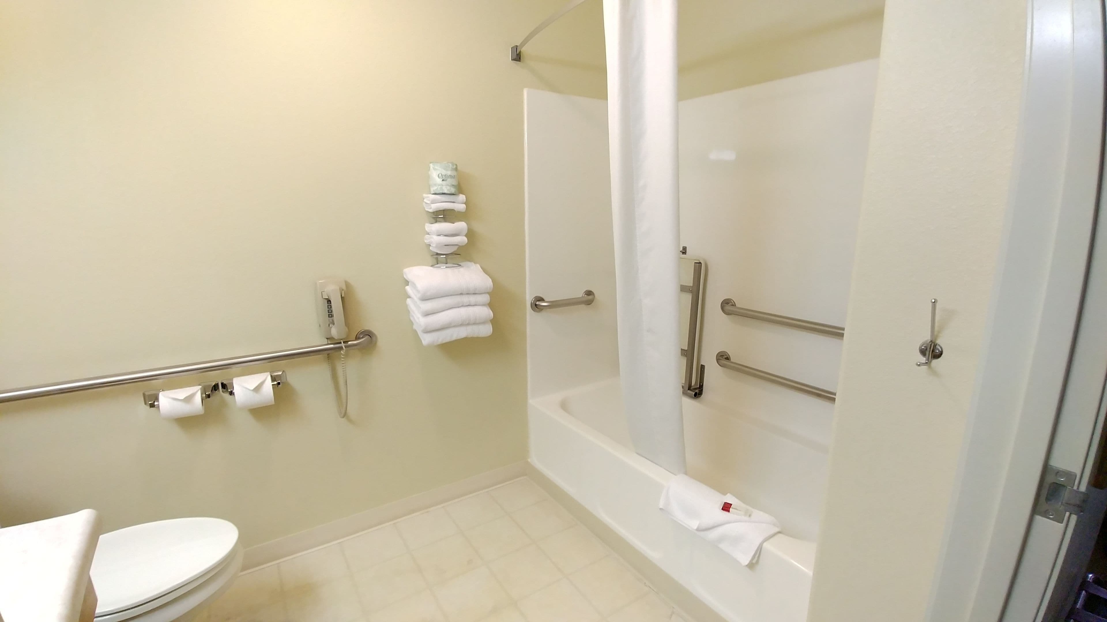 Un baño con inodoro, ducha con barras de apoyo y secador de manos.