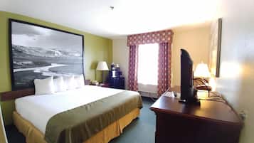 A hotel room with a large bed, a desk with a television, a window with curtains, and a painting on the wall.