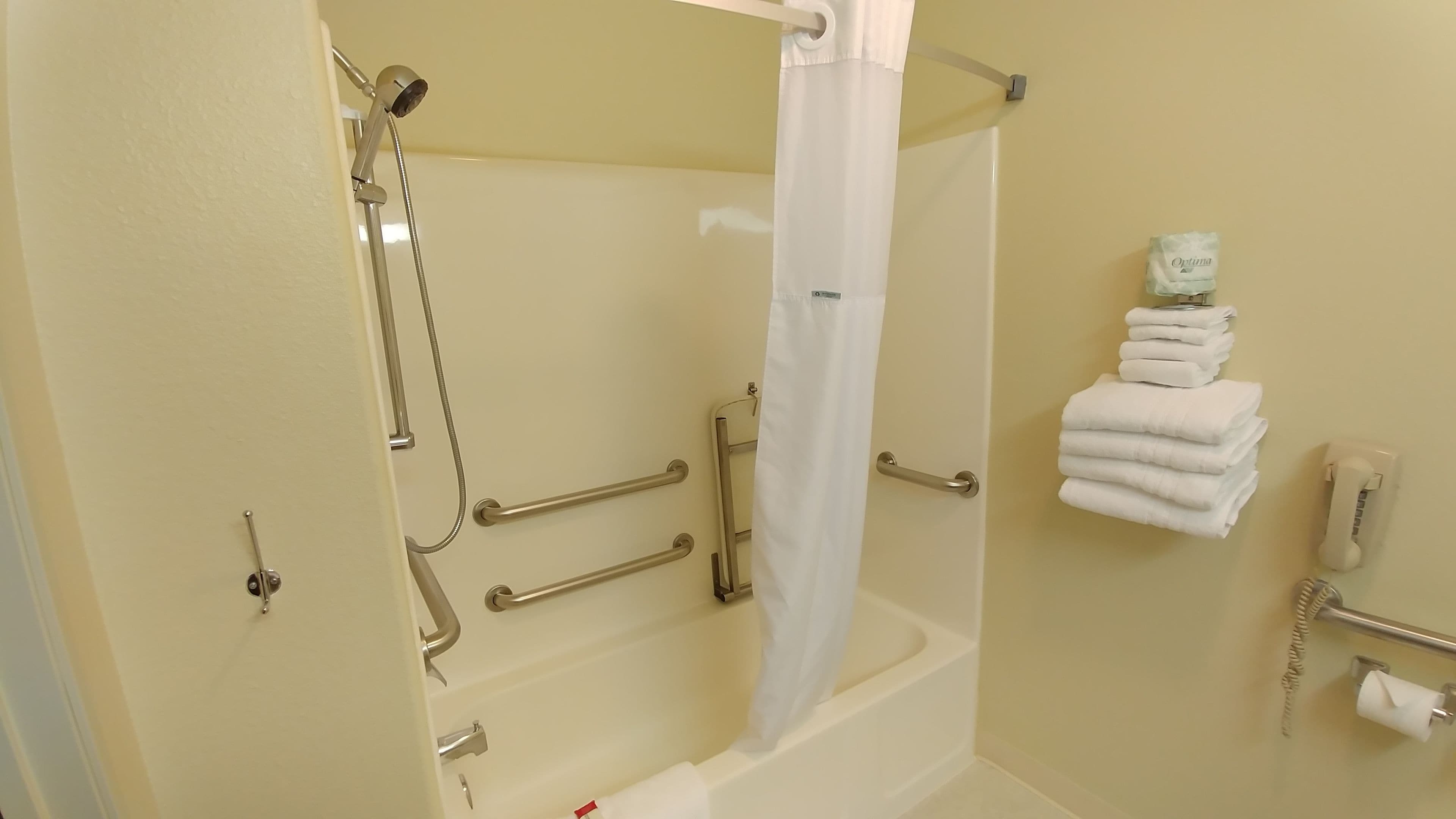 A bathroom with a bathtub, shower, grab bars, a toilet, a towel rack, and a telephone.