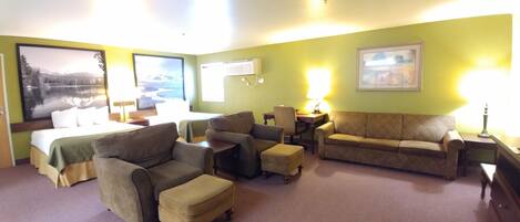 A hotel room with a bed, two sofas, a chair, a small table, and a desk.