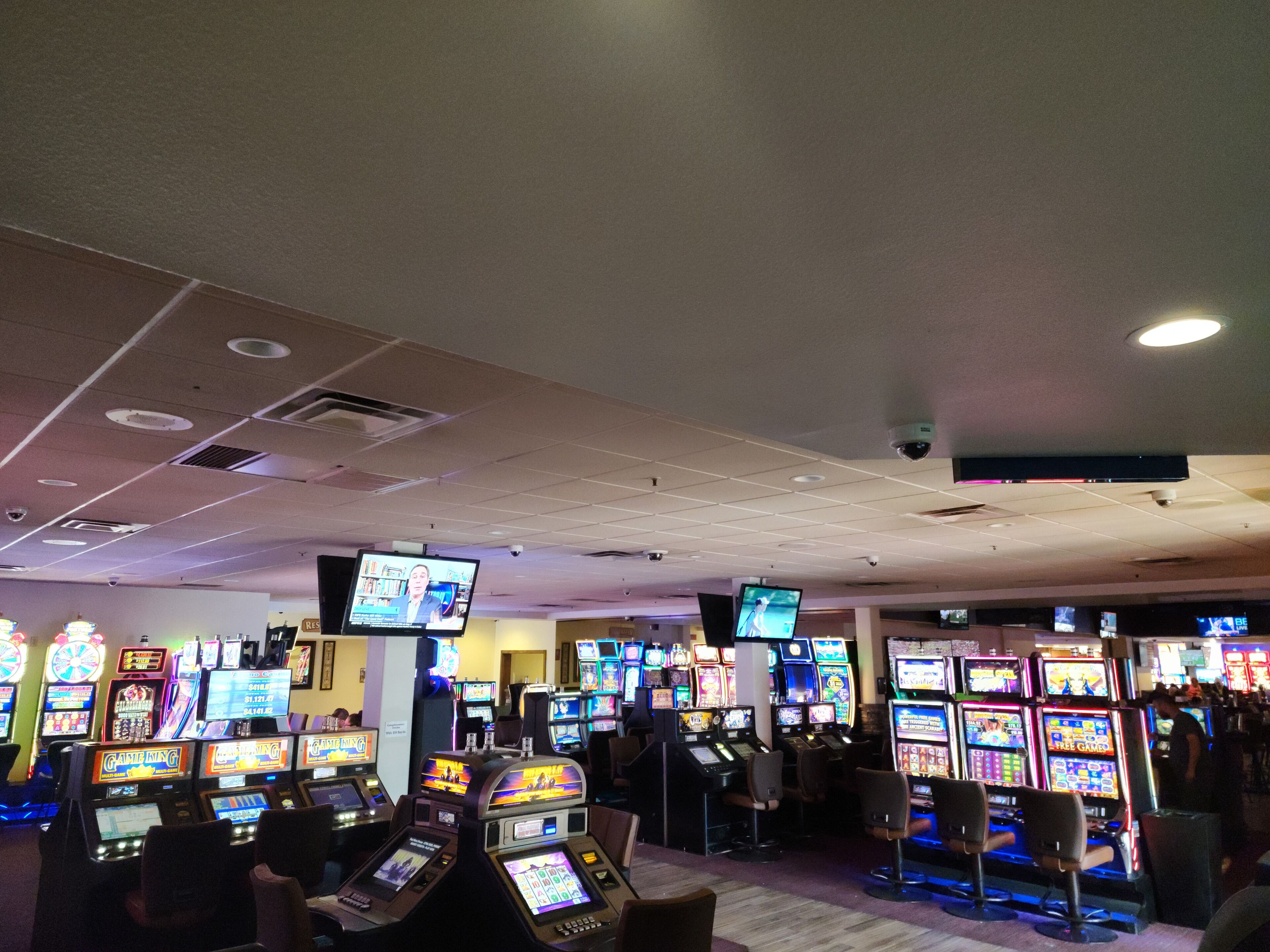 A casino with multiple slot machines and a few people playing.