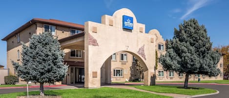 Un edificio con una entrada en arco característica, un letrero azul que indica que es un Best Value Inn, y dos árboles de hoja perenne en su fachada.