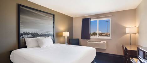 Habitación de hotel con una cama grande, un escritorio, una silla, un ventanal con vistas y aire acondicionado instalado en la pared.