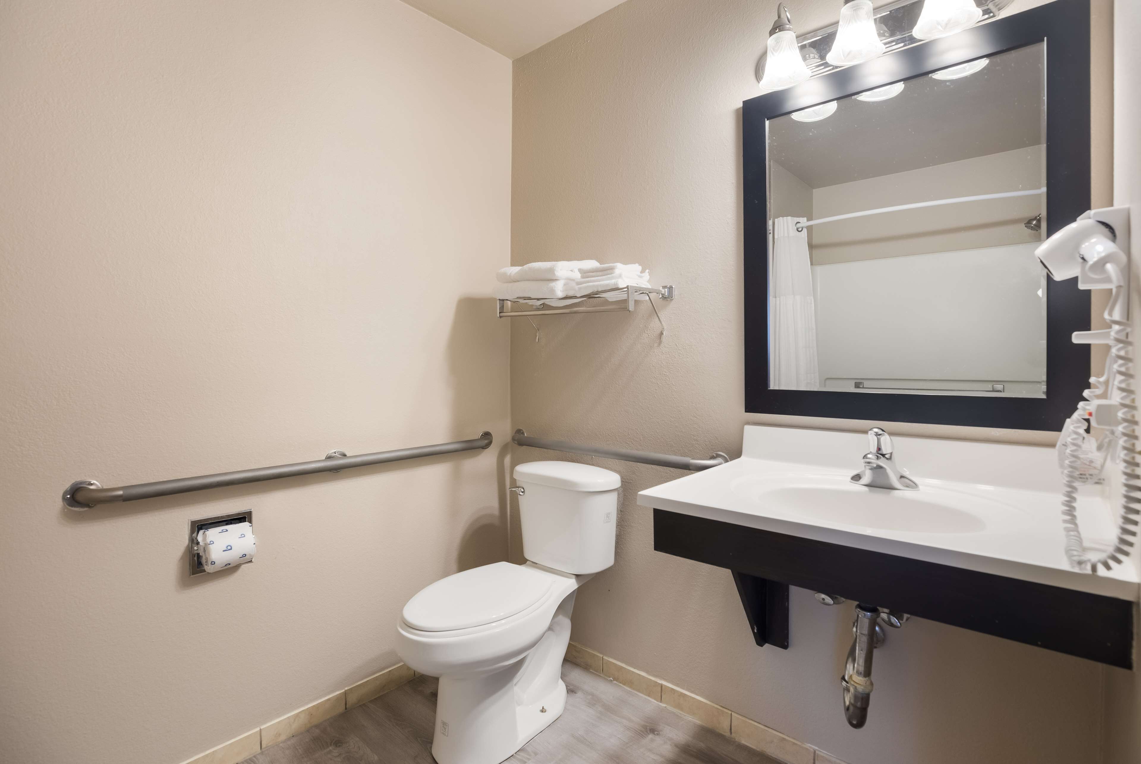 Une salle de bain avec des toilettes blanches, un lavabo avec un miroir, un porte-serviettes et un sèche-mains.