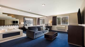 A modern hotel room with a large bed, a sofa, a coffee table, a TV, and a large window with curtains.