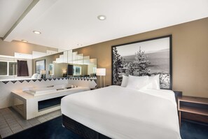 A modern hotel room with a large bed, a built-in bathtub, a large mirror, and a view of a snowy landscape. - Americas Best Value Inn Sparks (Sparks)