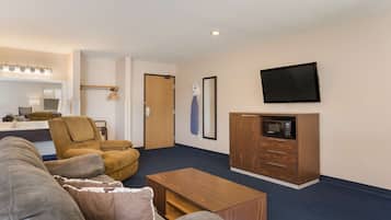 Een moderne woonkamer met een bank, een houten salontafel, een aan de muur bevestigde televisie en een magnetron in een houten kast.
