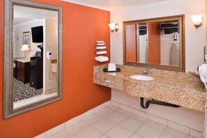 A bathroom with a granite countertop, a sink, a mirror, and a towel rack. - Hotel Heritage (El Monte)