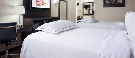A hotel room with two beds, a desk, a chair, a TV, and a mirror.