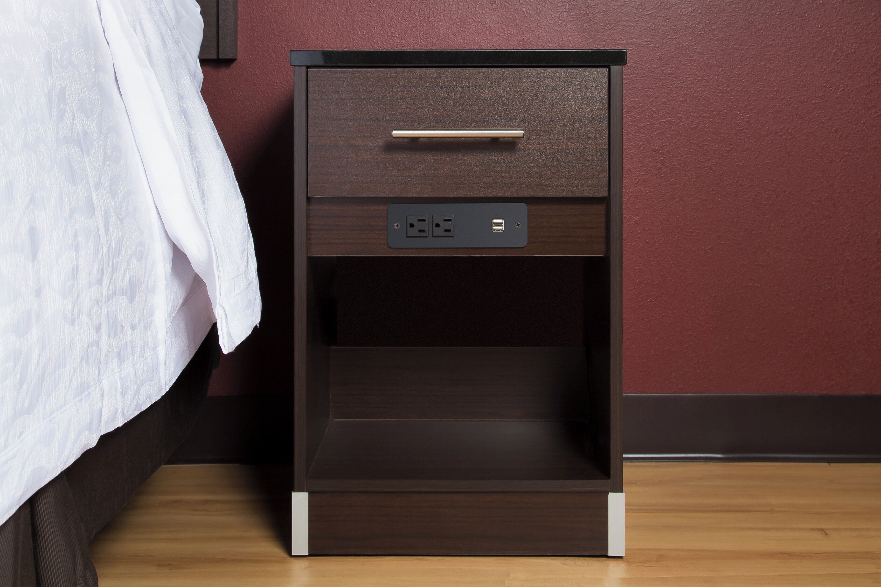 A wooden bedside table with a drawer and a power outlet.