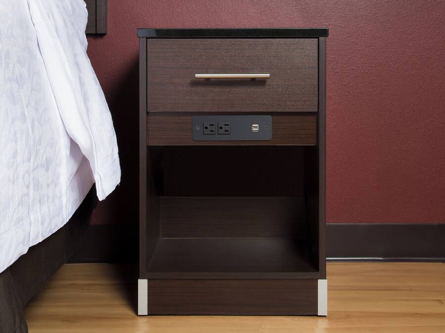 A wooden bedside table with a drawer and a power outlet.