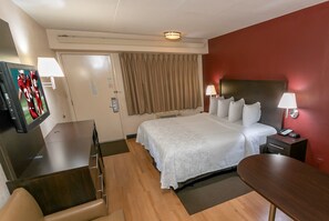 Habitación de hotel con cama, escritorio, silla, televisor y mesita de noche con lámpara.