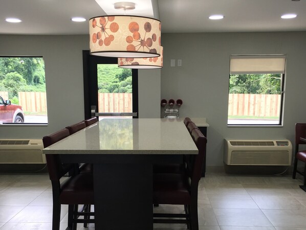 A dining area with a large table, chairs, a ceiling light fixture, and windows with views of a backyard and a vehicle. - Red Roof Inn PLUS+ Birmingham East - Irondale/ Airport (Birmingham)
