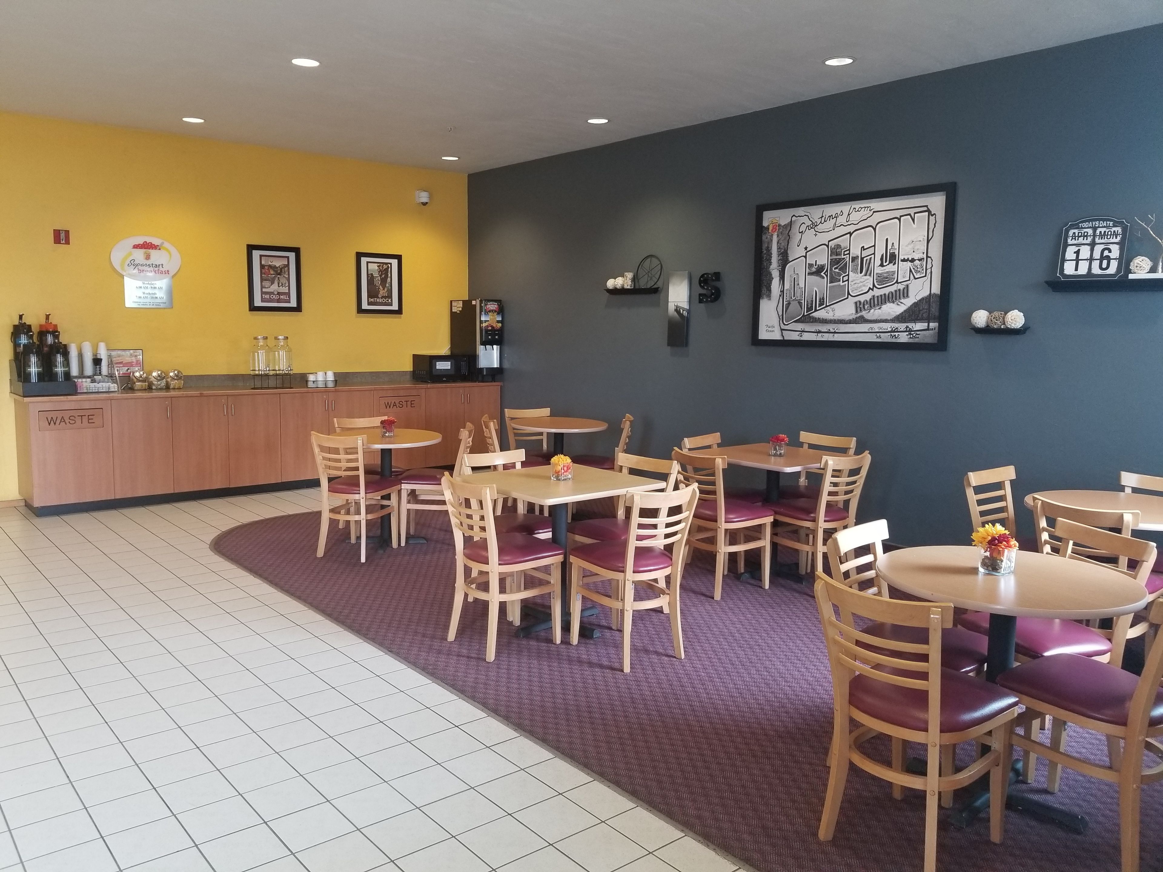 Ein Restaurant mit Holztischen und -stühlen, einer Theke mit einer Kaffeemaschine und gerahmten Kunstwerken an den Wänden.