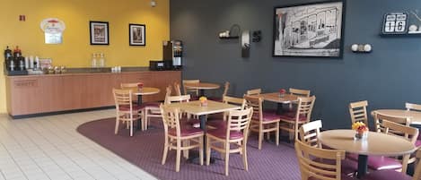 Ein Restaurant mit Holztischen und -stühlen, einer Theke mit einer Kaffeemaschine und gerahmten Kunstwerken an den Wänden.