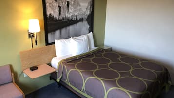 Una camera d'albergo con un letto, un comodino, una lampada, una sedia e un quadro appeso al muro.