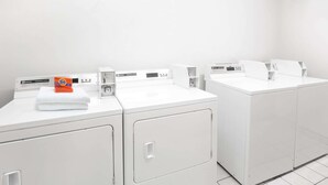 Un cuarto de lavandería con varias lavadoras y secadoras, un panel de control y una caja de detergente Tide.