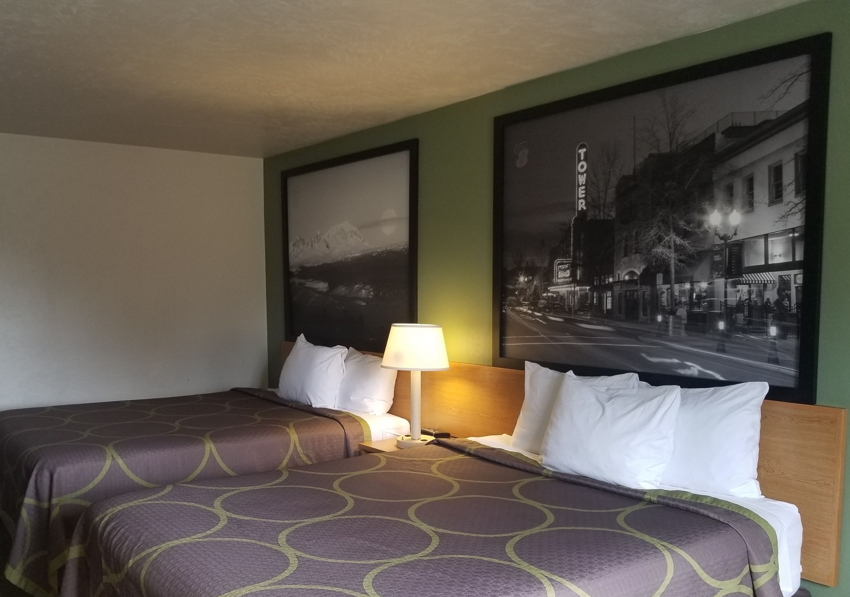 Una habitación de hotel con una cama, una mesita de noche, una lámpara y dos cuadros en la pared.
