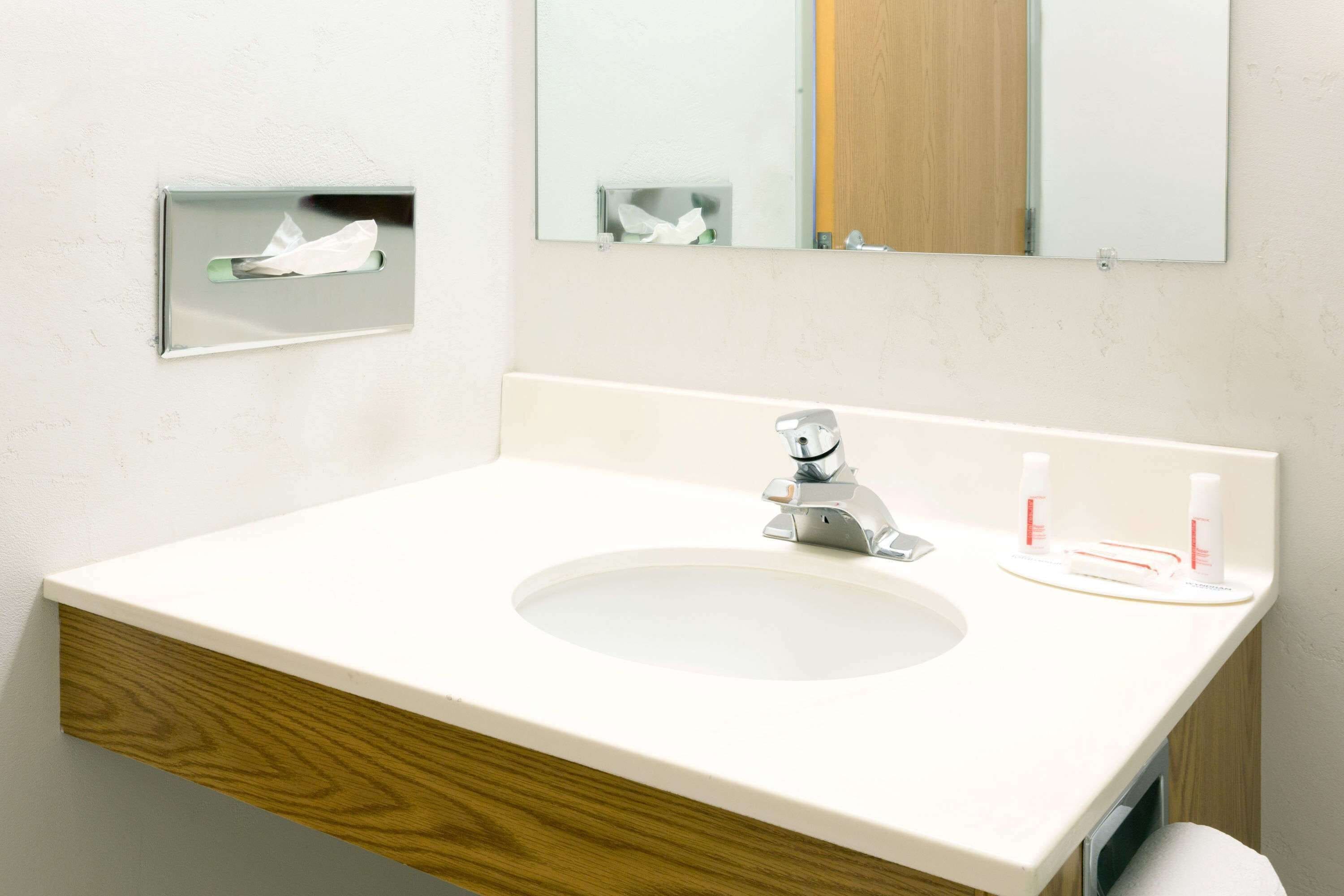 Ett badrum med ett vitt handfat, en spegel och en kommod i trä.