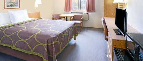 A hotel room with a bed, a desk with a computer, a chair, a TV, and a window with curtains.