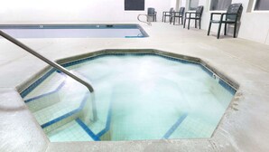 Una piscina interior con borde de azulejos, una escalera metálica y varias sillas a lo largo de la pared.