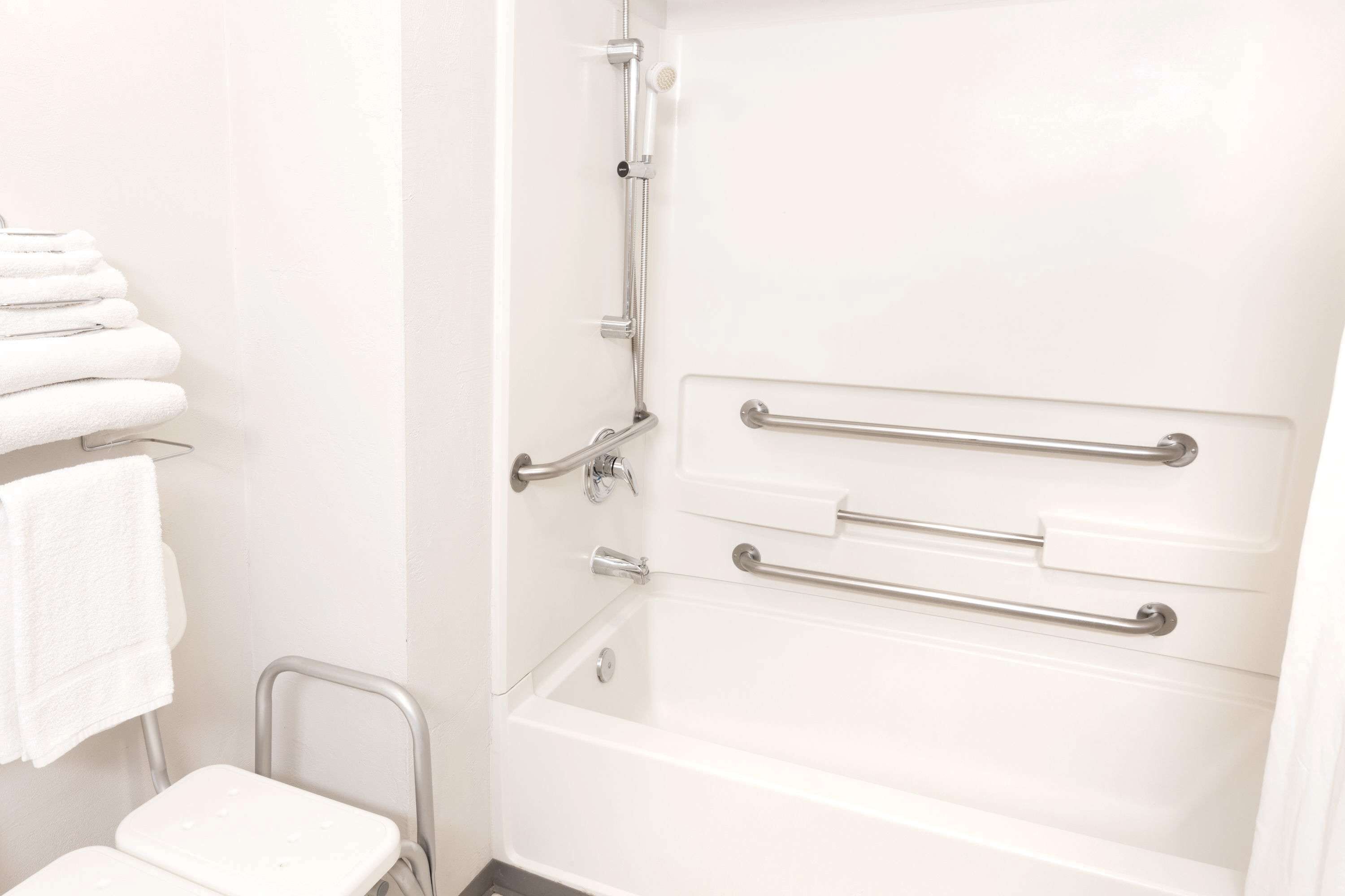 A white bathroom with a bathtub, grab bars, and a white towel rack.