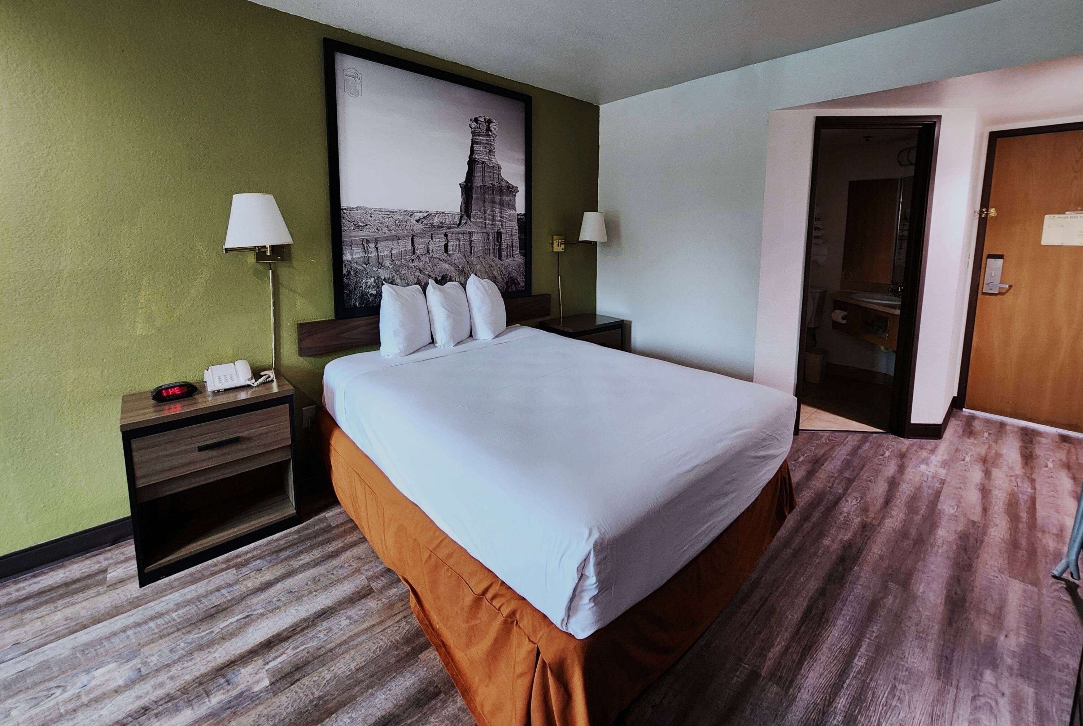 A hotel room with a large bed, two bedside tables, a nightstand, a lamp, and a framed picture on the wall.
