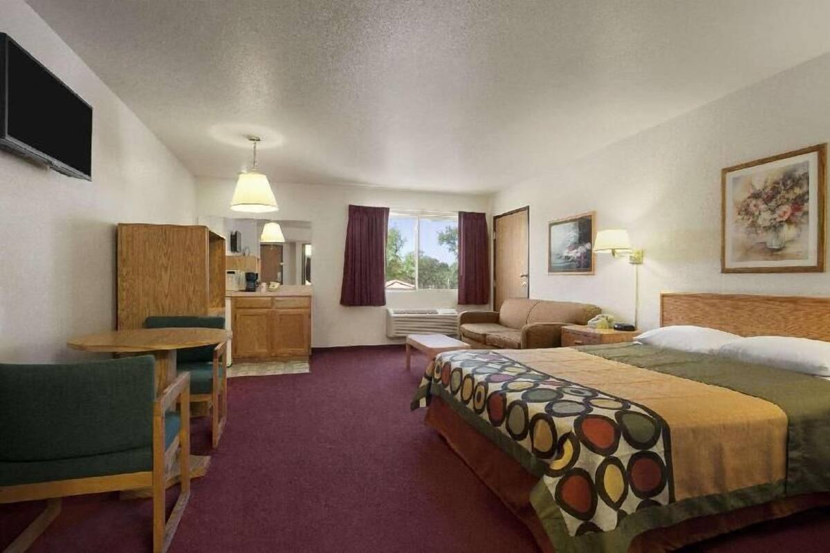 Ein Hotelzimmer mit Bett, Schreibtisch, Sessel, Sofa, Fernseher, Fenster mit Vorhängen und einem Bild an der Wand.