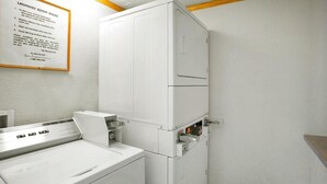 A laundry room with stacked washers and dryers, a white wall, and a framed laundry room rules sign. - FairBridge Inn Express Merrillville (Merrillville)