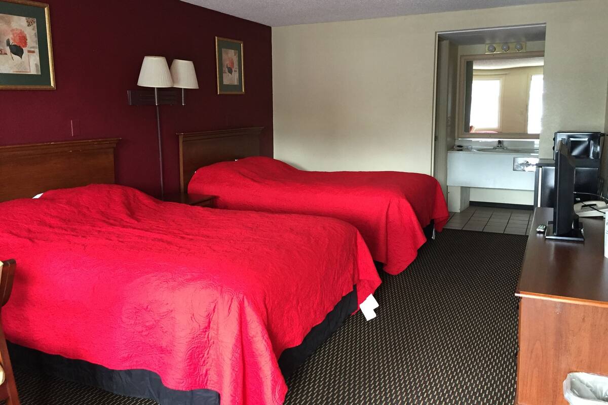 Habitación de hotel con dos camas, un escritorio, una lámpara y una ventana.