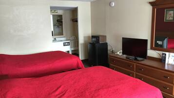 A hotel room with two beds, a television, a refrigerator, a dresser, and a mirror.