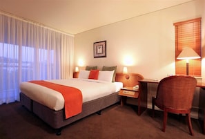 Une chambre d’hôtel avec un lit, une table de chevet, une lampe, une chaise et une fenêtre avec des rideaux.