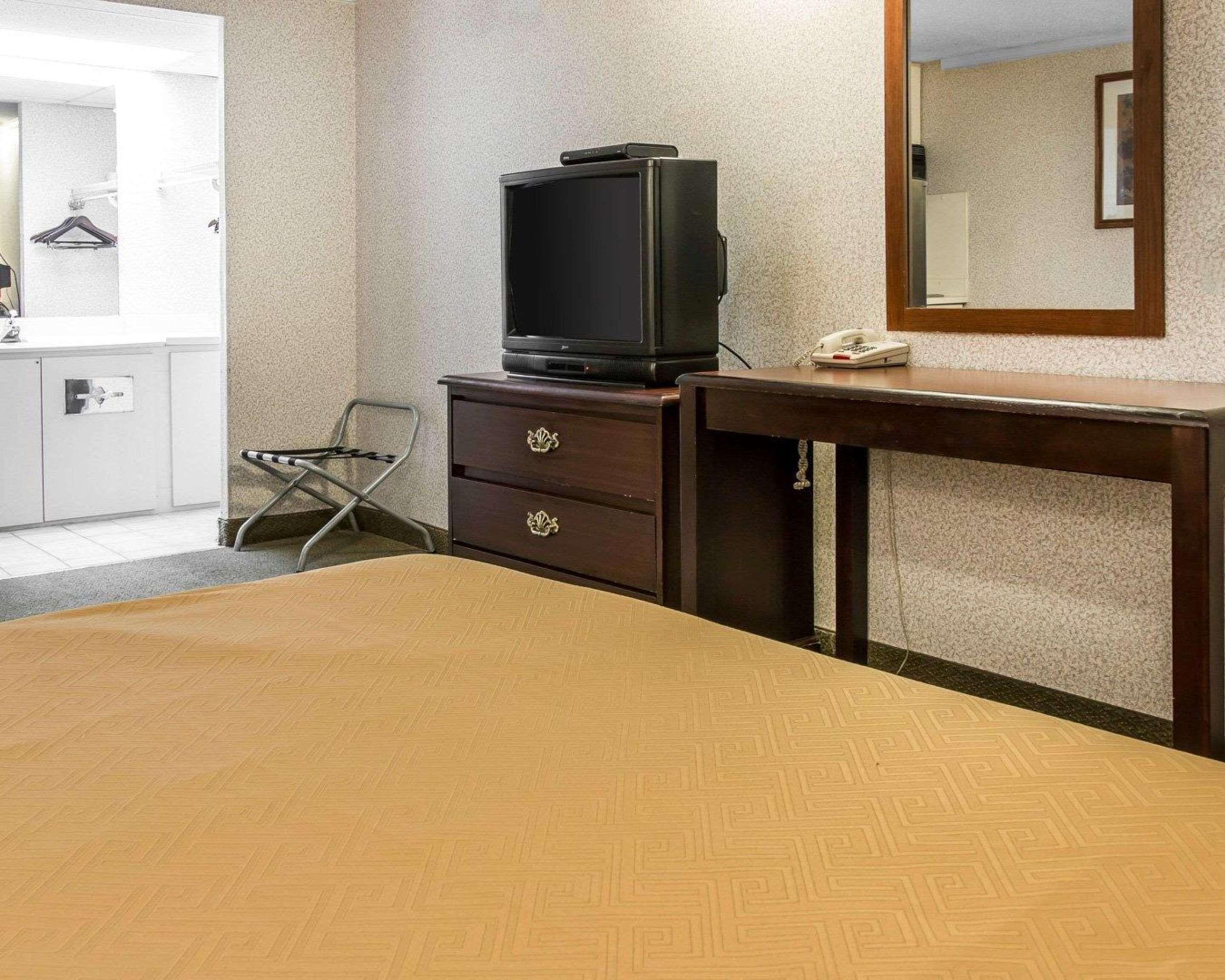 Quarto de hotel com cama, cómoda de madeira com televisão, espelho e telefone.